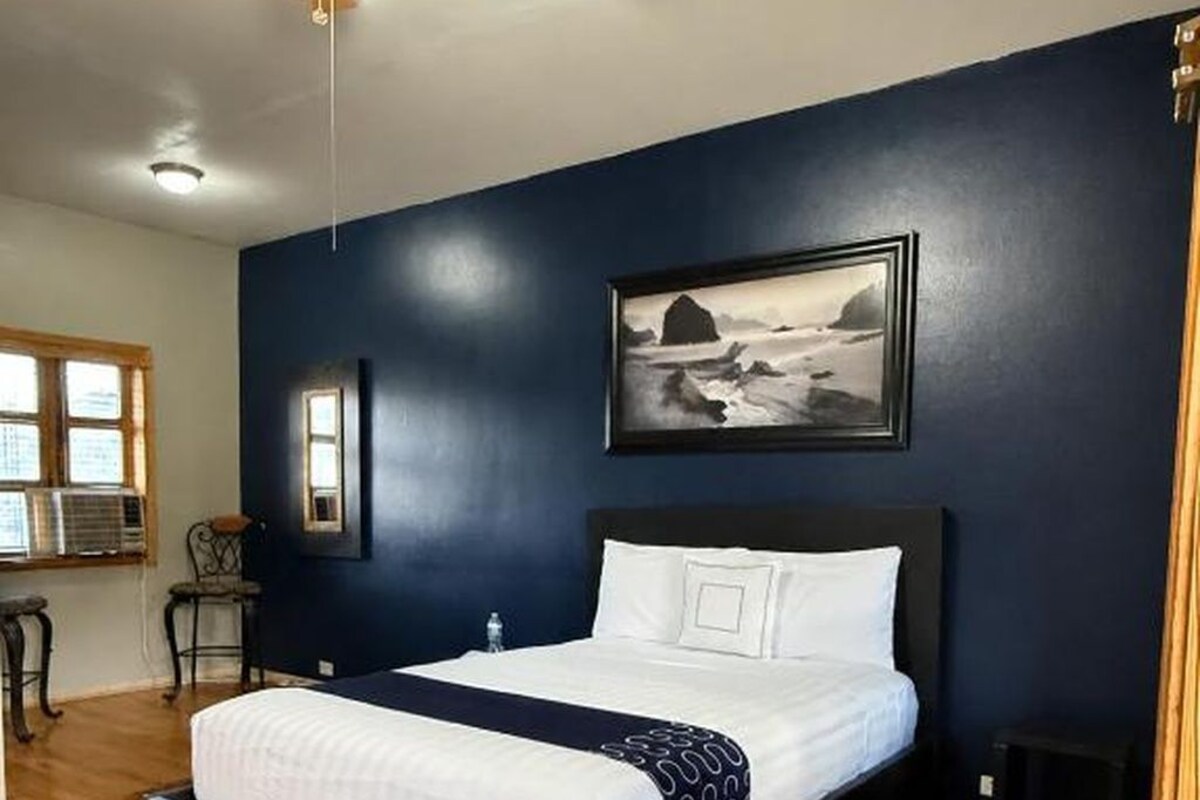 Une chambre à coucher avec un lit, un ventilateur de plafond, une fenêtre et un tableau accroché au mur.
