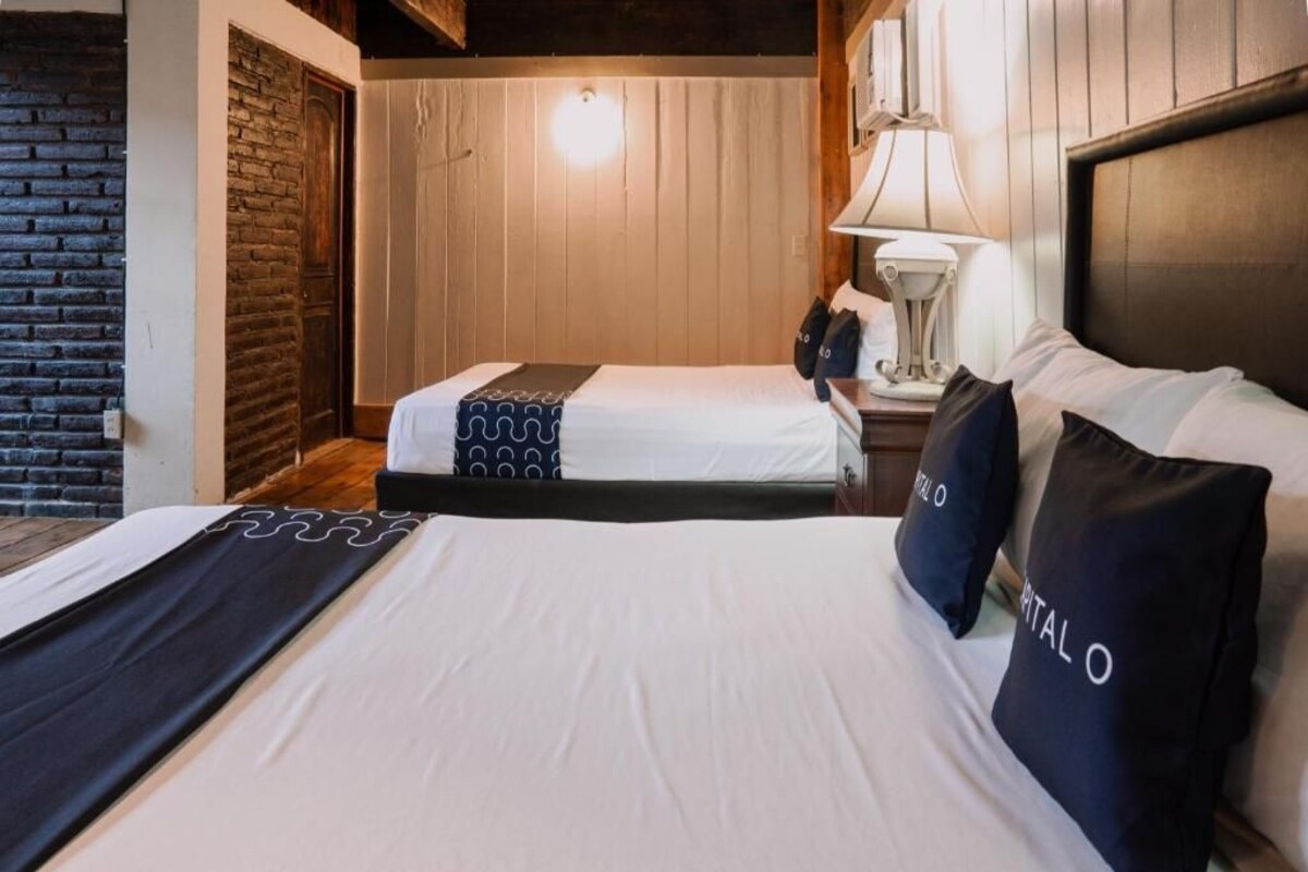 Une chambre d’hôtel avec deux lits, un mur en bois, un mur en briques et une table de chevet avec une lampe.