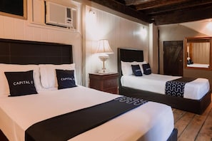 Une chambre d’hôtel avec deux lits, chacun doté d’une tête de lit noire et de draps blancs. Une table de chevet avec une lampe se trouve entre les deux lits.