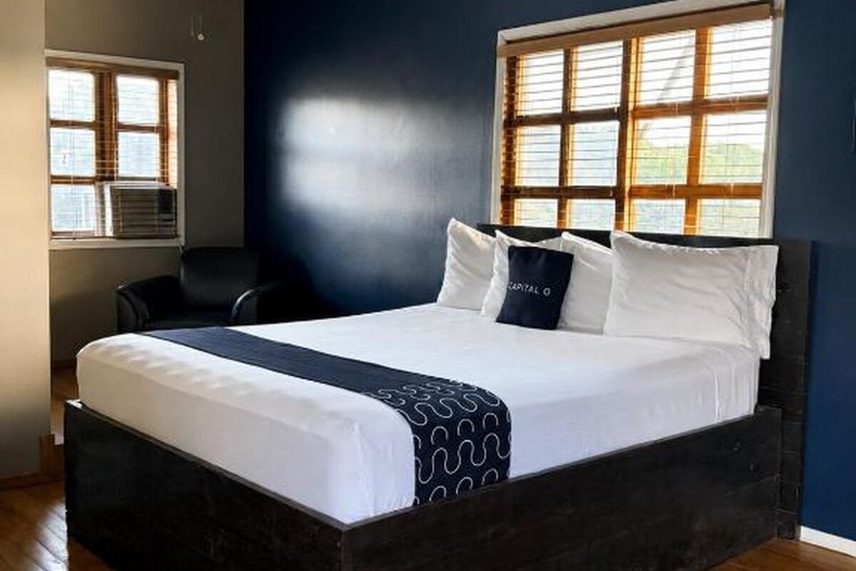 Une chambre avec un grand lit, un ventilateur de plafond et une fenêtre avec des stores.