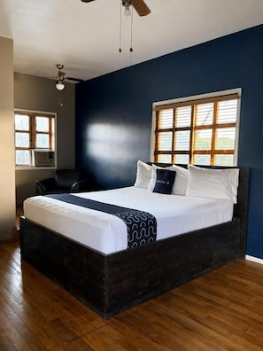 Une chambre avec un grand lit, un ventilateur de plafond et une fenêtre avec des stores.