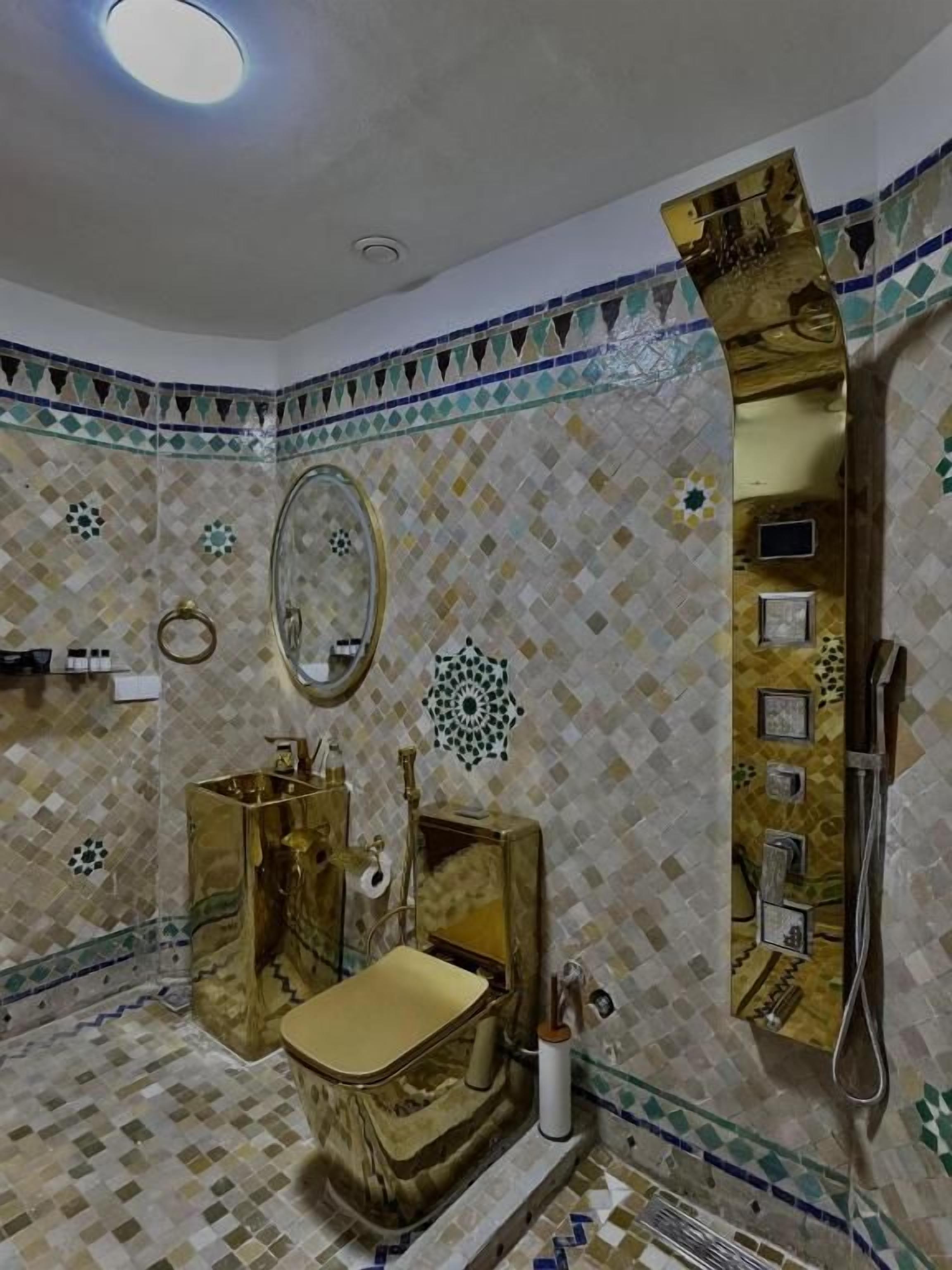 A bathroom with a gold toilet, a sink, a mirror, and a shower.
