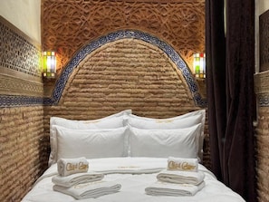 Ein Hotelzimmer mit einer Wand im Ziegelsteinmuster, einem Bett mit weißer Bettwäsche und einem dekorativen Bogen über dem Bett.