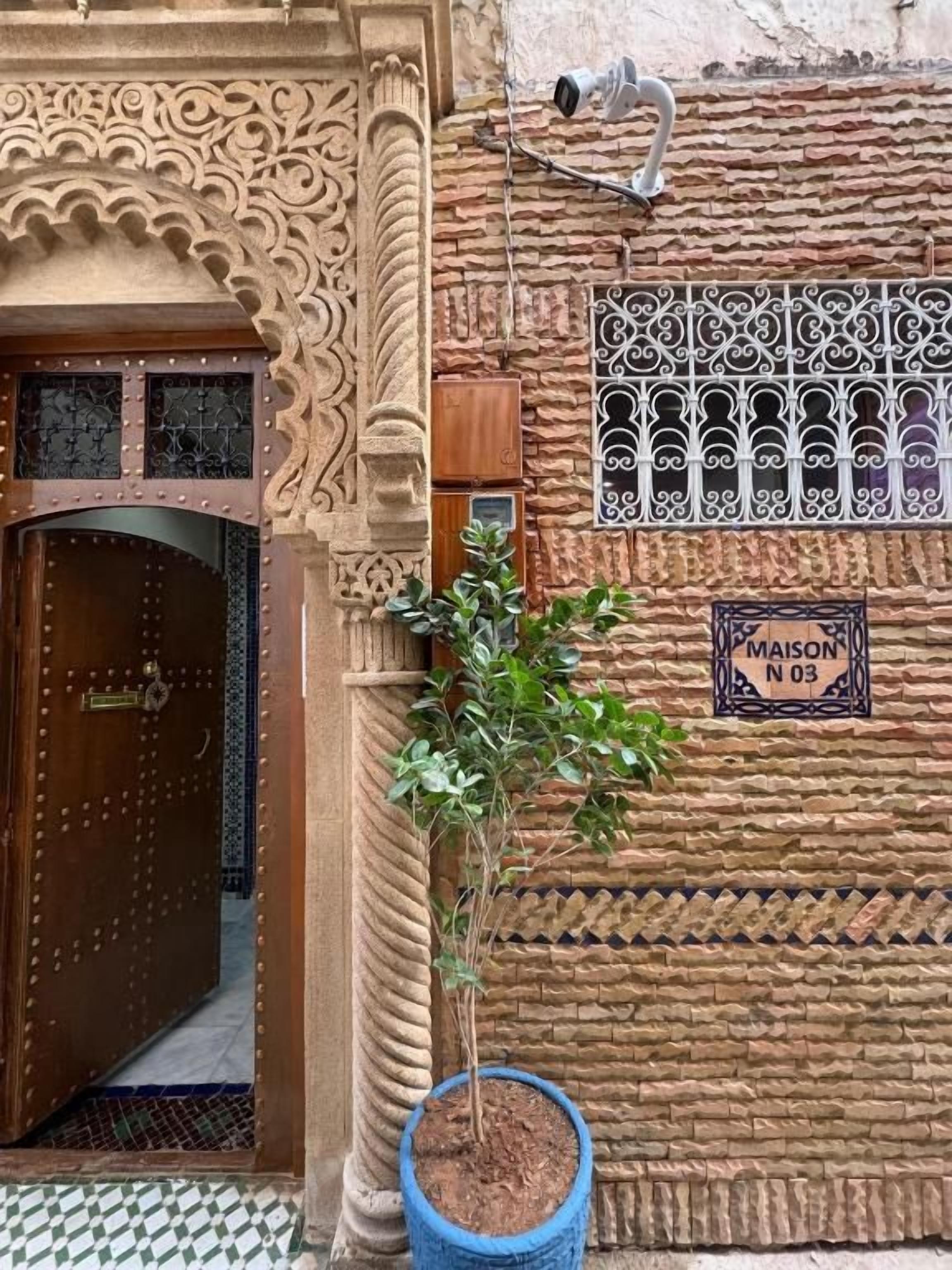 A traditional Moroccan building with a wooden door, intricate stone carvings, and a potted plant.