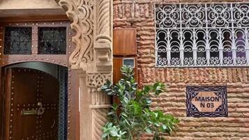 A traditional Moroccan building with a wooden door, intricate stone carvings, and a potted plant.