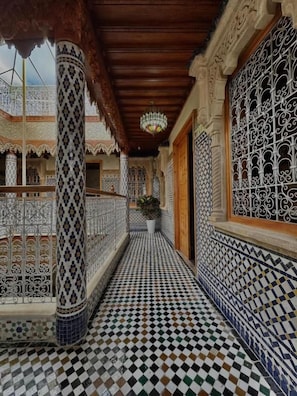 A corridor with patterned tiles, ornate columns, and a hanging chandelier. - RIAD ASSWAR (Rabat)