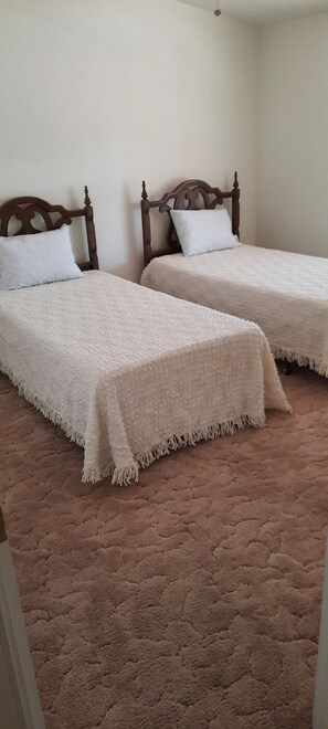 Ein Zimmer mit zwei Einzelbetten, jeweils mit einem Holz-Kopfteil und weißer Bettwäsche.