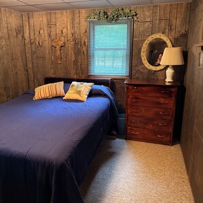 A bedroom with a wooden wall, a bed with blue bedding, a dresser, and a mirror with a decorative frame. - Cozy 2-bedroom cabin on Solberg Lake perfect for relaxing getaway. (Phillips)