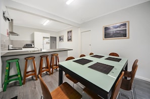 A modern kitchen with white cabinets, a microwave, and a stainless steel range hood. There are wooden stools and a dining table with chairs. - Hook, Wine & Linger on Learmonth (Portland)