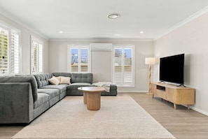 A modern living room with a sectional sofa, a round coffee table, and a TV on a wooden stand. - Morrisset Retreat - Sleeps 5, Walk to Bathurst CBD (Bathurst)