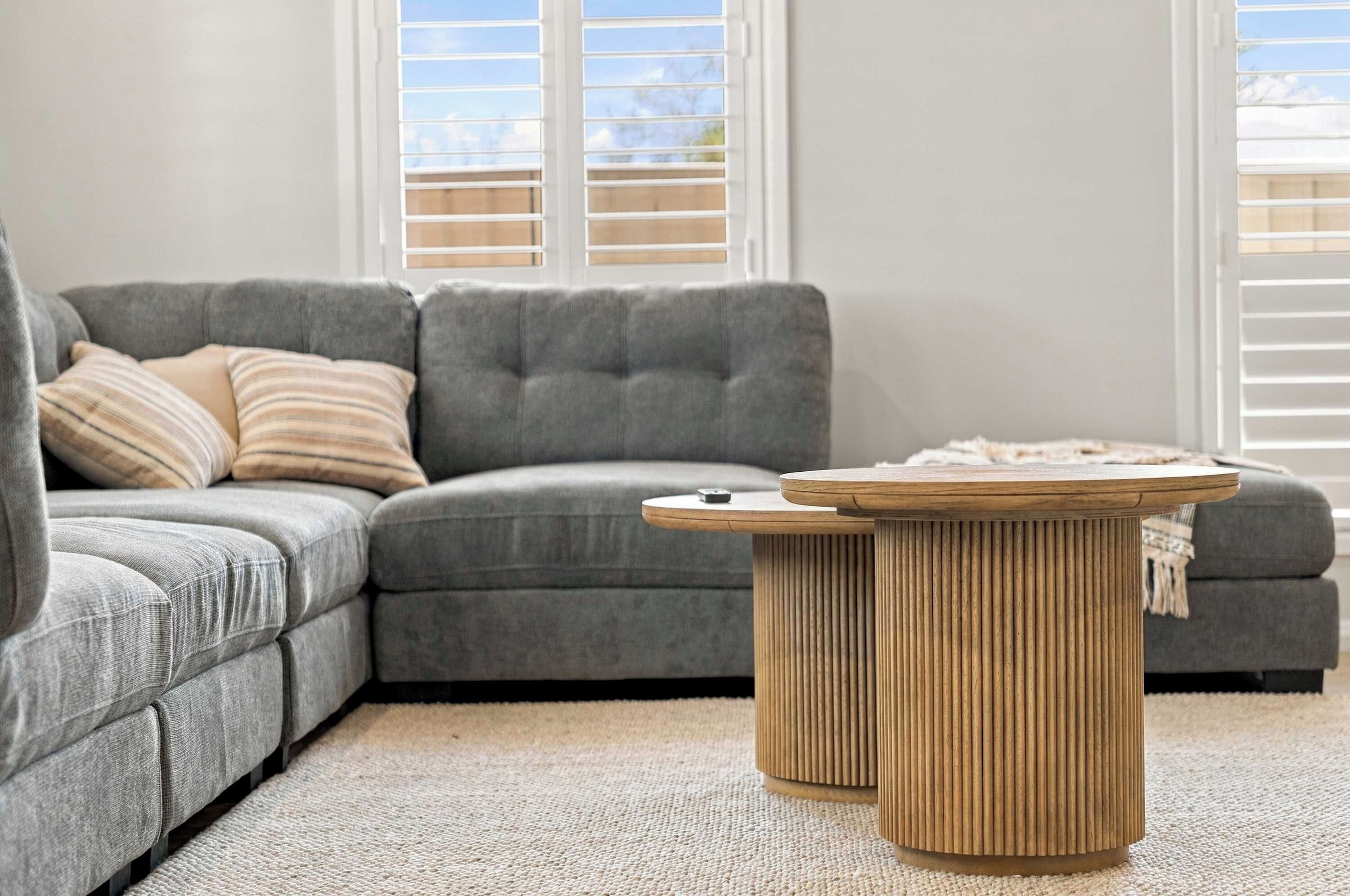 A grey sectional sofa with a striped pillow, a round wooden coffee table, and a light-colored carpet.