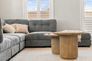 A grey sectional sofa with a striped pillow, a round wooden coffee table, and a light-colored carpet. - Morrisset Retreat - Sleeps 5, Walk to Bathurst CBD (Bathurst)