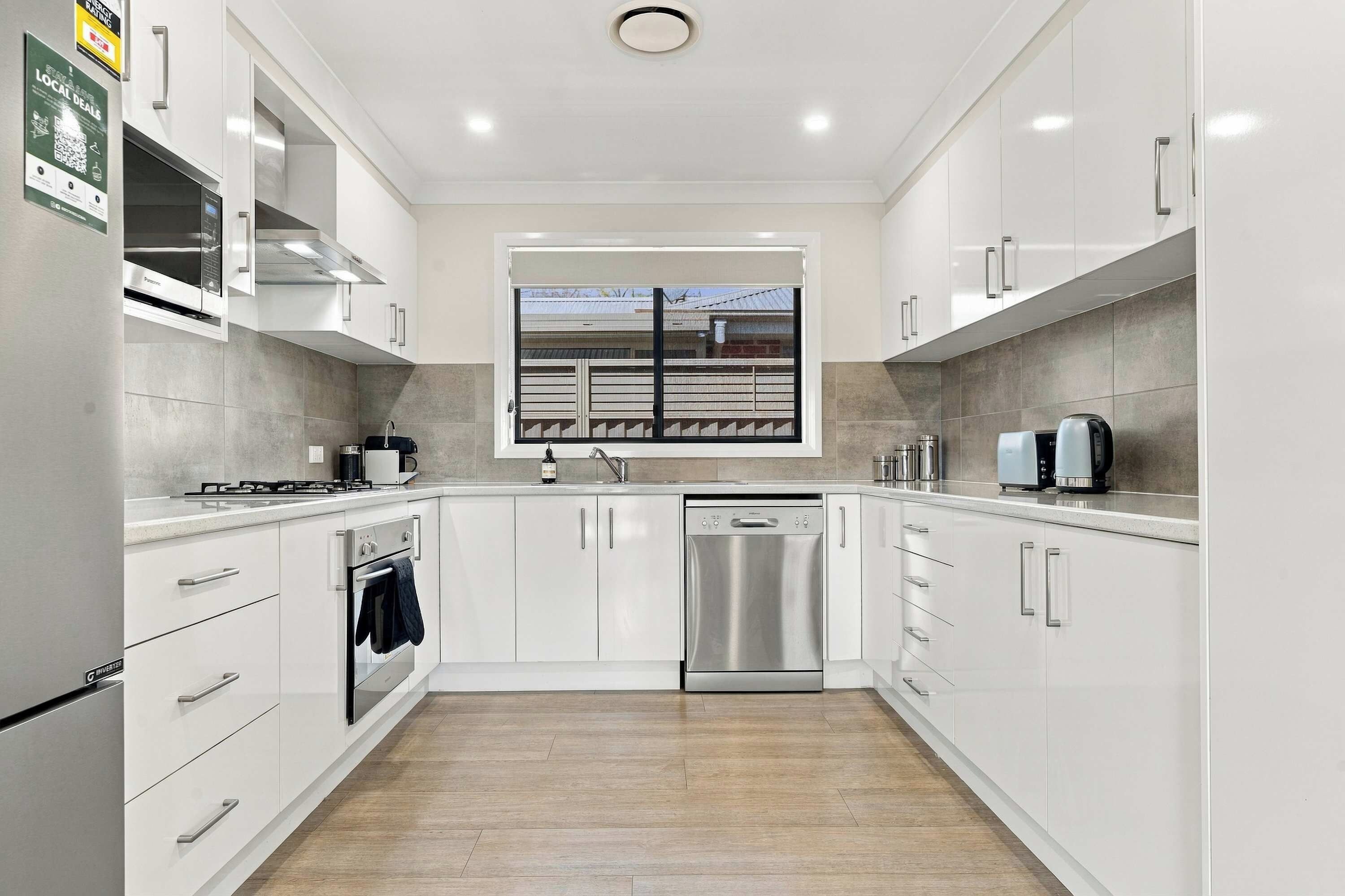 A modern kitchen with white cabinetry, stainless steel appliances, and a window with a view of a building.