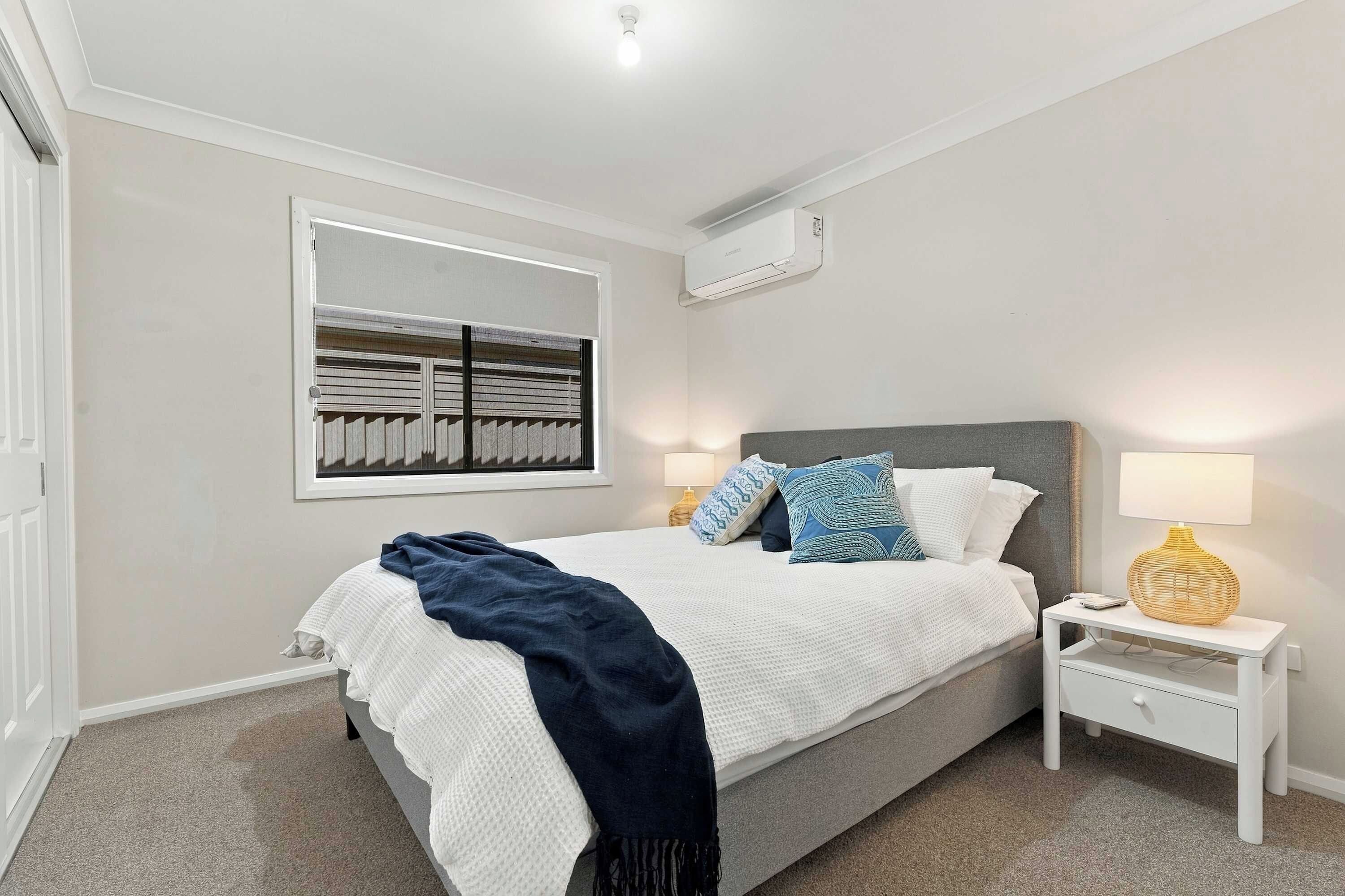 A bedroom with a bed, bedside tables, a lamp, and a window with blinds.