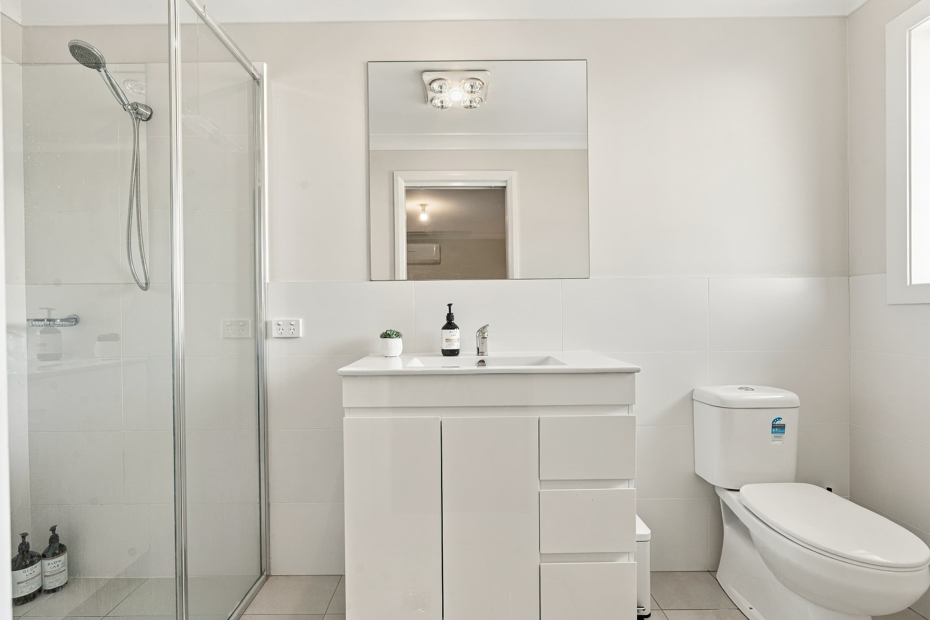 Ein modernes Badezimmer mit Duschkabine aus Glas, einem weißen Waschbecken mit Spiegel darüber und einer Toilette.