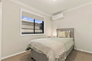 Ein Schlafzimmer mit einem Bett, einem Fenster mit Jalousien, einer Klimaanlage und einem Nachttisch mit Lampe.