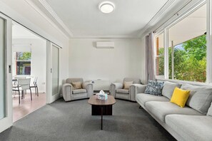 A modern living room with a grey sofa, two armchairs, a coffee table, and a large window with a view of greenery. - Bathurst Family Home - 3 Bed, Sleeps 6, Near Mount Panorama (Bathurst)