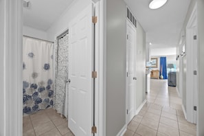 A hallway with white doors, a patterned shower curtain, and a tiled floor. - Oceanview Condo - Huge Deck Overlooking Ocean with Pool! (Carolina Beach)