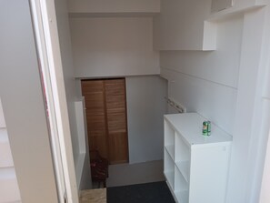 Passadís estret amb una porta de fusta, una estant blanca amb una conserva i una petita cadira.