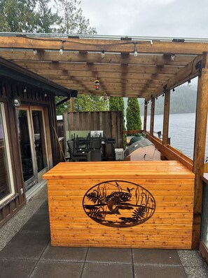 A wooden outdoor seating area with a grill and a decorative metal fish sculpture. - The Captain at Secret Bay Hideaway (Private Oceanfront Cottage with Moorage) (Egmont)