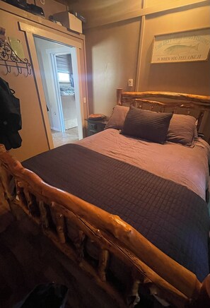 A bedroom with a wooden headboard, a bed with a quilted cover, a nightstand, and a wall-mounted sign. - The Captain at Secret Bay Hideaway (Private Oceanfront Cottage with Moorage) (Egmont)