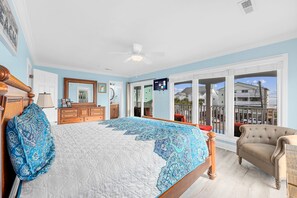 A bedroom with a large bed, a dresser, a chair, and a television. - A Little Piece of Heaven - Colorful 5BR w/ Ocean-View Porches & Shared Pool (Walk to Beach) (North Myrtle Beach)