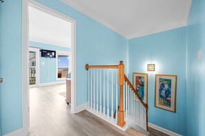 Um corredor com paredes azul claro, escada de madeira com balaústres brancos e duas obras de arte emolduradas na parede.