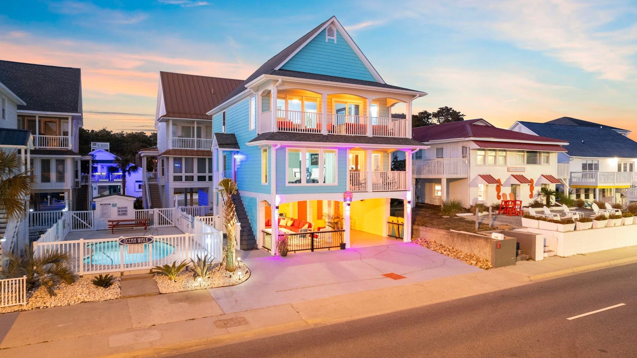 A two-story house with a balcony, a pool, and a beach-themed exterior.