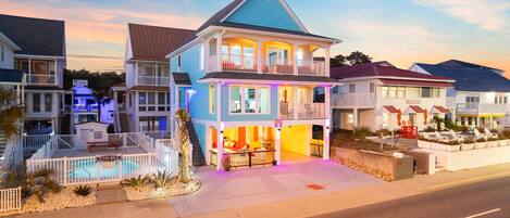 A two-story house with a balcony, a pool, and a beach-themed exterior.