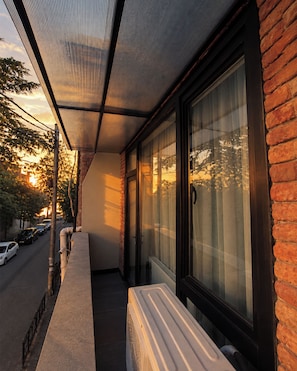 Un espacio exterior cubierto con un banco, una ventana con cortinas y una pared de ladrillo.