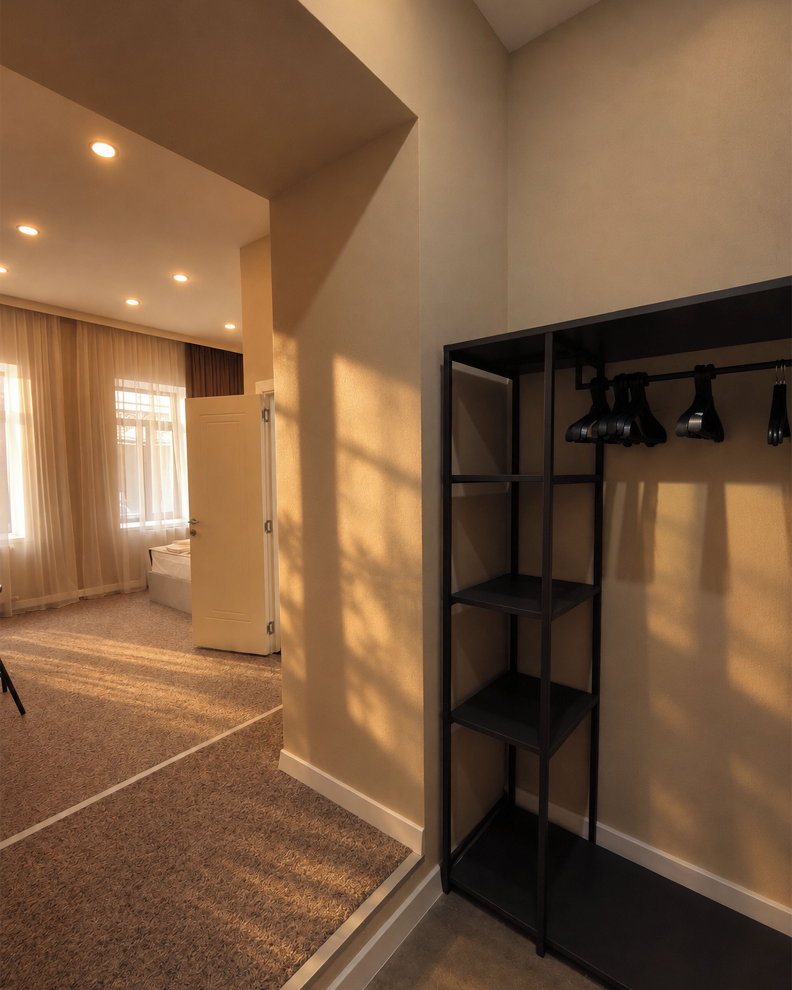 A room with a carpeted floor, a door, a shelf unit, and a window with curtains.