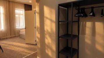 A room with a carpeted floor, a door, a shelf unit, and a window with curtains.