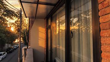 A balcony with a view of parked cars and trees, a brick wall, and a window with blinds.