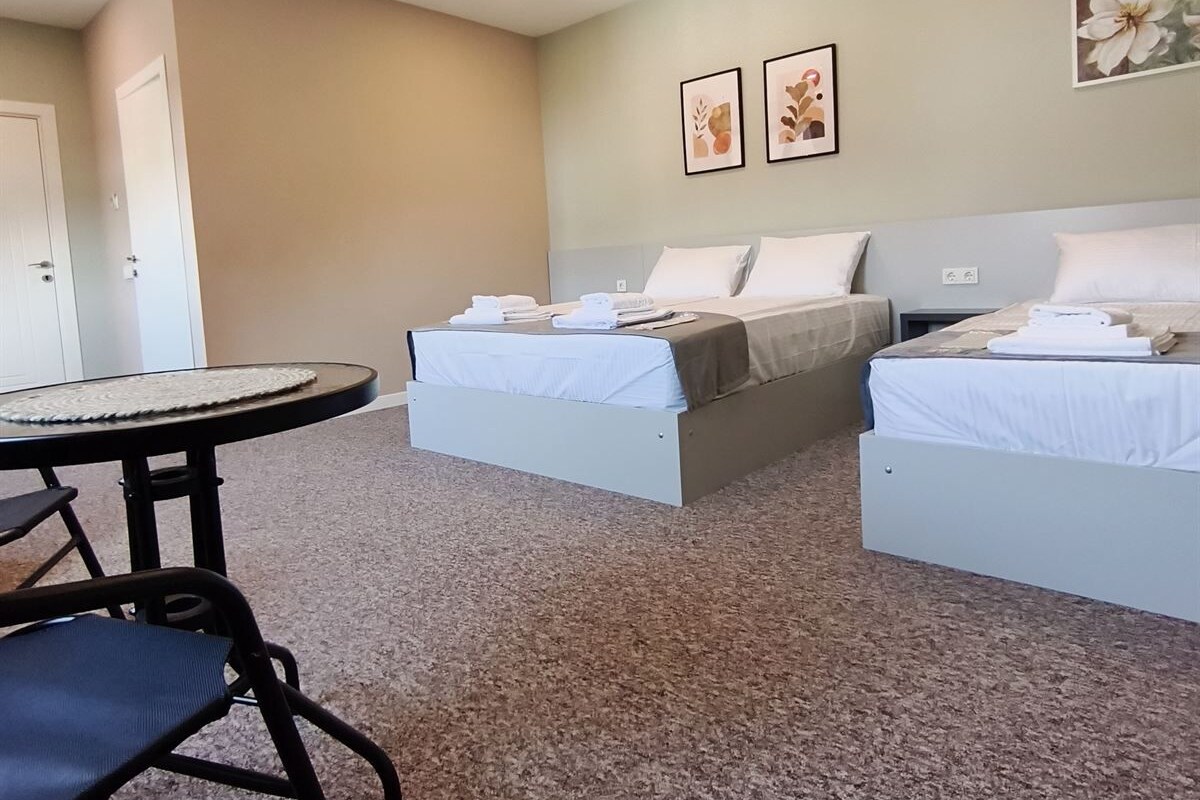 Quarto de hotel com duas camas, uma mesa redonda e uma cadeira.