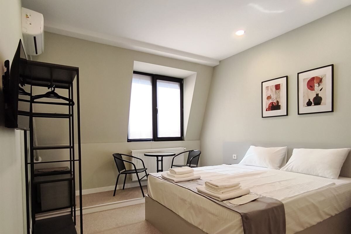 Quarto com cama, escrivaninha, cadeiras, radiador e janela.