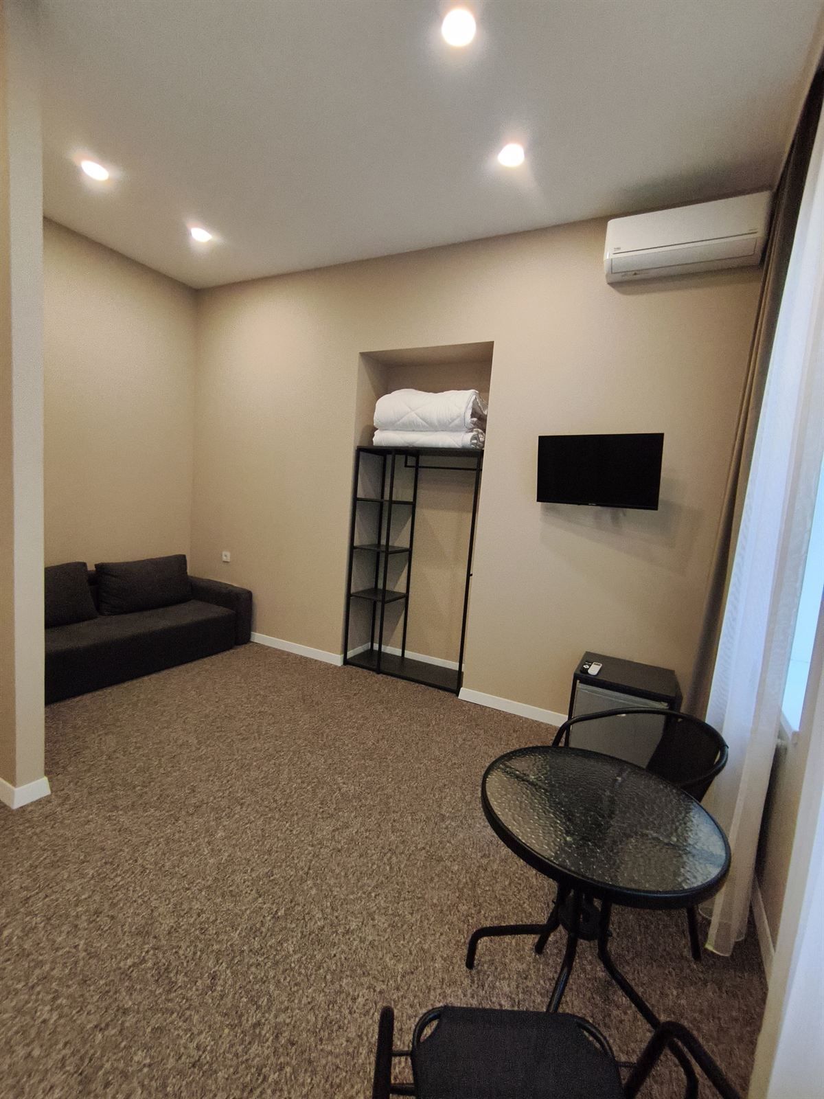 Quarto com sofá, pequena mesa com cadeiras, televisão fixada na parede e beliche com cobertor dobrado.