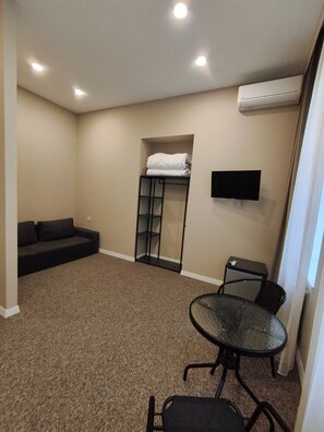 Quarto com sofá, pequena mesa com cadeiras, televisão fixada na parede e beliche com cobertor dobrado.