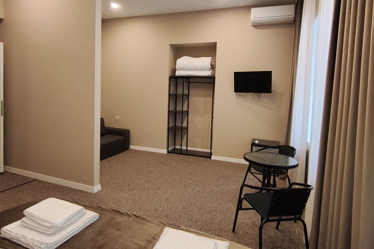 Quarto de hotel com cama, escrivaninha, cadeira, televisão e armário.