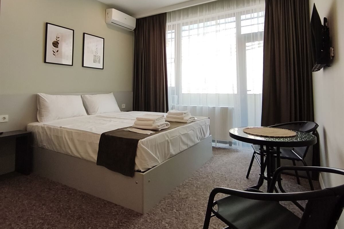 Quarto de hotel com uma cama, uma mesinha redonda, uma cadeira e uma televisão fixada na parede.