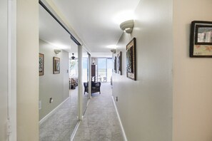A hallway with framed artwork on the walls, a carpeted floor, and a door leading to a room with a bed and a window. - Enjoy stunning Gulf views from this beachfront Sanibel condo - Lighthouse Point 223 (Sanibel Island)