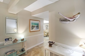 A hallway with a mirror, framed artwork, a decorative wall piece, and a console table with a lamp. - Enjoy stunning Gulf views from this beachfront Sanibel condo - Lighthouse Point 223 (Sanibel Island)