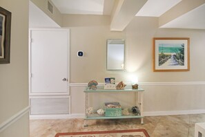 A hallway with a white door, a thermostat, a welcome sign, a framed picture, and a glass console table with decorative items. - Enjoy stunning Gulf views from this beachfront Sanibel condo - Lighthouse Point 223 (Sanibel Island)