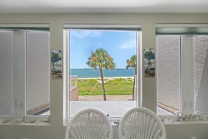 A room with a view of the beach, two white chairs, and a window with a view of palm trees and the sea. - Enjoy stunning Gulf views from this beachfront Sanibel condo - Lighthouse Point 223 (Sanibel Island)