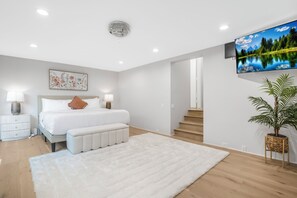 A modern bedroom with a bed, bedside lamps, a fluffy rug, a large window with a scenic view, and a television mounted on the wall. - Mulholland Ridge By Alora Reserve (Los Angeles)