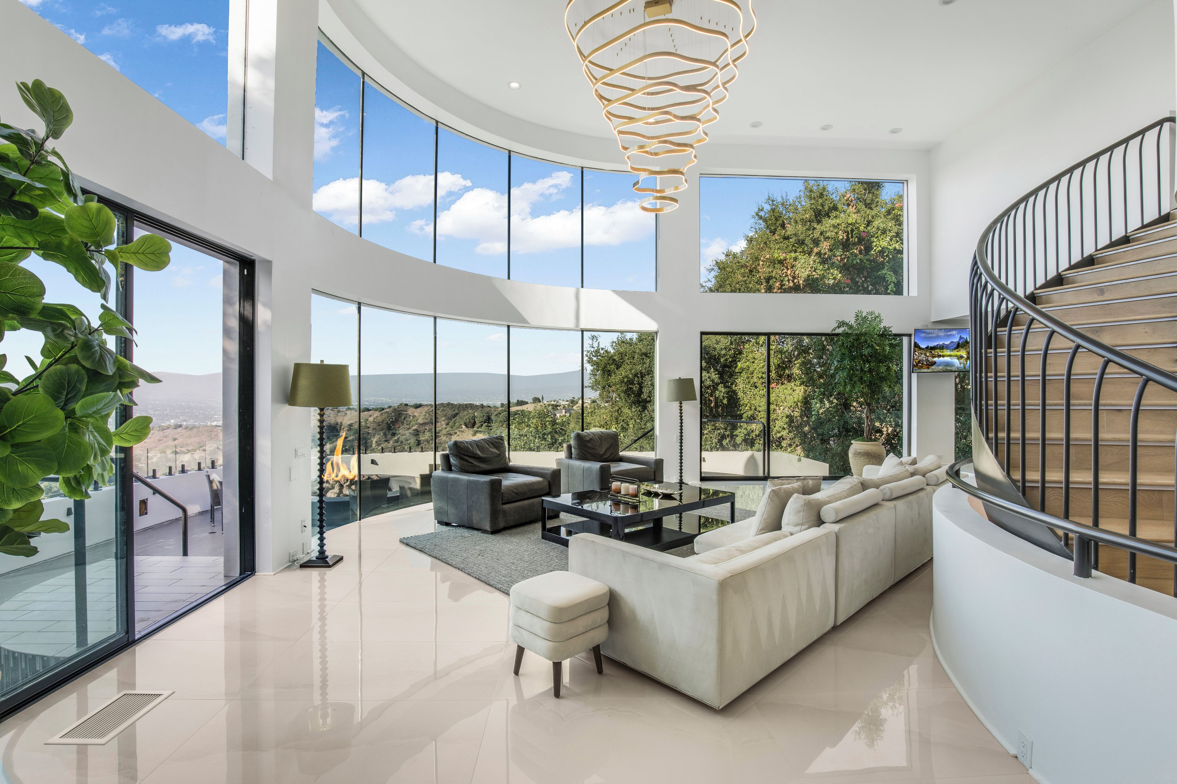 A spacious living area with a large window, a modern chandelier, and a staircase.