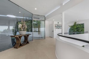 A modern reception area with a glass partition, a wooden console table with a potted plant, and a curved reception desk. - Mulholland Ridge By Alora Reserve (Los Angeles)
