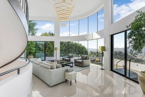 A modern interior with a curved staircase, a large white sofa, and a view of the outdoors. - Mulholland Ridge By Alora Reserve (Los Angeles)