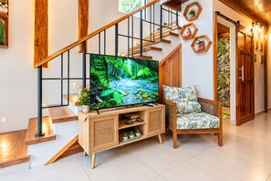 Ein modernes Wohnzimmer mit einer Holztreppe, einem Flachbildfernseher auf einer Holzkonsole, einem Korbstuhl und einer Wand mit sechseckigen Regalen.