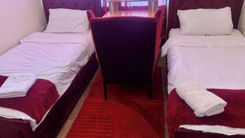 A hotel room with two single beds, a red rug, and a small table with a chair.