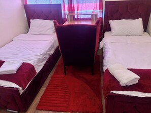 A hotel room with two single beds, a red rug, and a small table with a chair. - Apartment Sleeps 5 With Wifi (Wolverhampton)